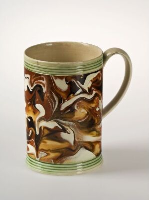  A ceramic mug with a marbled pattern in shades of brown, white, and black, bordered by sage green stripes at the top and bottom, resting on a light background.