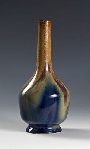  An elegant vase featuring an amber glaze that transitions from caramel to bronze on the slender neck, blending into a rich, sea-like palette of blues and greens on the bulbous base, grounded by a dark navy or black foot.