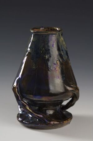  A small, glossy, iridescent ceramic vase with an uneven, organic shape, showcasing hues of dark blue, purple, and green against a light-to-dark gray gradient background. Artist name and title are unknown.