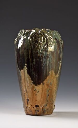  A handcrafted vase with a glossy black and silver glaze dripping over the top, transitioning to an unglazed beige, textured surface with a few small holes, set against a neutral gray background.