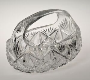  A crystal cut glass basket with intricate designs on an oval body, featuring a smooth curved handle, against a light grey background.