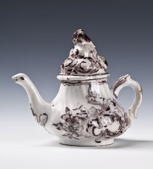  An ornately decorated monochromatic porcelain teapot with baroque-style grayish-black floral and figure designs on a white background. The teapot has a curved spout, a decorative handle, and a detailed lid with a finial on top.