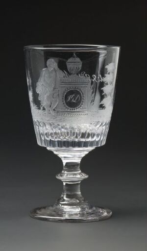  A transparent glass goblet with a wide, bell-shaped bowl and an ornate stem stands against a dark grey background. The goblet features an etched coat of arms within a border at its upper half, surrounded by intricate decorative patterns, suggesting historical significance or fine craftsmanship.