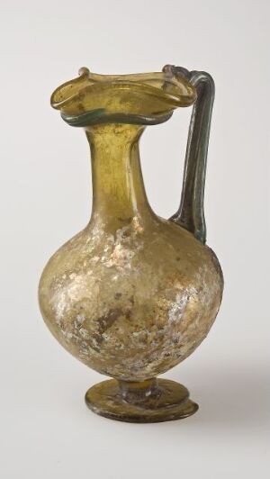  A vintage, hand-blown glass pitcher known as "kanne" by an unknown artist, displaying a yellowish-amber hue with a mottled pattern and a wide, undulating rim, a curvy handle, and a solid circular base.