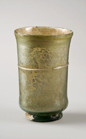  An antique cylindrical green glass vase with a tapered shape and a slightly lighter rim, displaying a textured, weathered surface, indicative of its age and handcrafted nature.