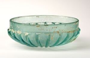  A translucent, shallow glass bowl with a pleated exterior design and a pale turquoise color, displaying some areas of residue or aging on its surface.