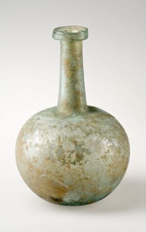  An opaque, ancient glass vessel with a bulbous base and a slender neck featuring muted greens and off-whites with a mottled and iridescent surface, suggesting historical significance.