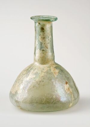  An aged glass flask with a broad, rounded base and a short neck, featuring subtle green and off-white colors with hints of iridescence and textural marks indicative of antiquity, set against a plain background.