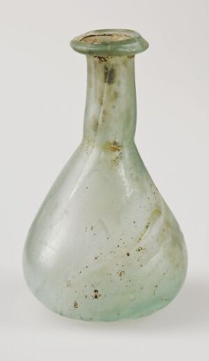  An antique green glass bottle with a bulbous base and a narrow neck, showing signs of age such as a mottled appearance, bubbles within the glass, and irregularities at the rim.