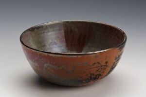  A simple, earthy-colored bowl with a rust-red to dark brown exterior and a muted graphite-grey interior, resting on a neutral gray background with soft lighting accentuating its smooth contours. Artist name and title are unknown.