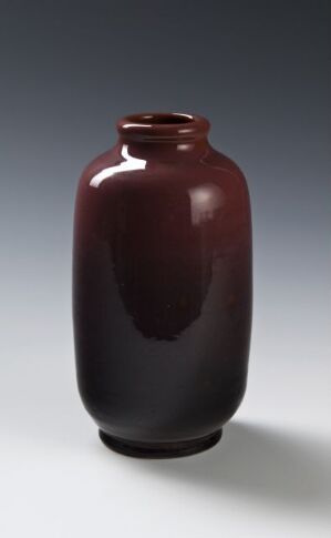  A glossy dark burgundy ceramic vase with a narrow base that widens and then tapers to a short neck on a light grey gradient background.