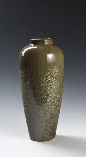  A tall, slender vase with a glossy finish, featuring a metallic bronze upper section and a speckled granite-like lower section, set against a gradient background shifting from dark grayish-blue to light gray.