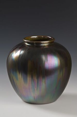  An iridescent vase with a bulbous body and a narrow neck, exhibiting a rainbow-like sheen with patches of purple, blue, pink, green, and orange against a dark background.