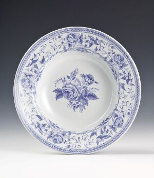  A traditional flintware plate with white lead glaze and blue transfer print decoration featuring central floral motifs and a bordered design of interlinked flowers and vines.