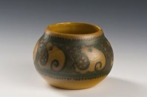  A small, round ceramic bowl with a glossy golden interior and a green and rust-patterned exterior featuring large paisley motifs, displayed against a graduated gray background.