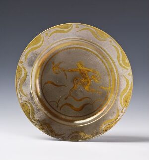  A decorative round dish with a marbled pattern of slate gray, yellow, and brown hues, featuring a golden rim and a centric abstract swirl that could evoke the semblance of an animal or character, set against a neutral light gray background.