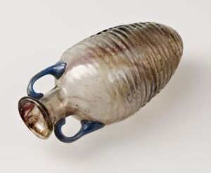  An ancient Roman glass flask with horizontal ridges, transitioning from frosted light to amber tones, featuring opaque blue looped handles on the narrow neck.