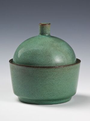  A green glazed ceramic container with a dome-shaped lid, featuring a small knob handle placed against a neutral gray background. The glaze has subtle speckling, providing a natural texture to the piece.