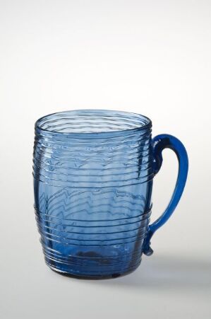  A translucent blue glass mug with spiral grooves and a solid blue handle, set against a neutral light grey-white gradient background. Artist name and title are unknown.