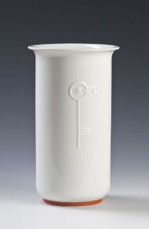  A cylindrical, white feldspar porcelain vase designed by Nora Gulbrandsen, with a flared opening, subtle embossed details, and an unglazed, terracotta-colored base against a muted blue-gray background.