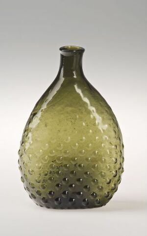  An olive-green glass bottle with a tapered neck and textured surface featuring small, round indentations, set against a neutral grey background. Artist name and title are unknown.