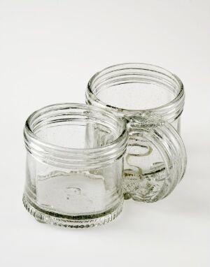  Two empty, clear glass jars with screw-top rims standing next to each other on a light-colored background.