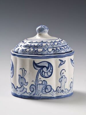  A ceramic sugar bowl with a lid, featuring off-white or cream color and ornate cobalt blue designs, reminiscent of traditional Delftware or Chinese porcelain, with a rounded knob on the lid.