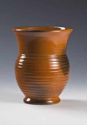  A warm, reddish-brown ceramic vase with horizontal striations on its surface, featuring a tapered neck and a flared lip. The color suggests a terracotta-like material, and the piece has an elegant, earthy appearance.