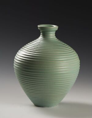  A glazed ceramic vase by Nora Gulbrandsen with a bulbous body and narrow neck, featuring horizontal ridges and a soft seafoam green color, set against a dark background.