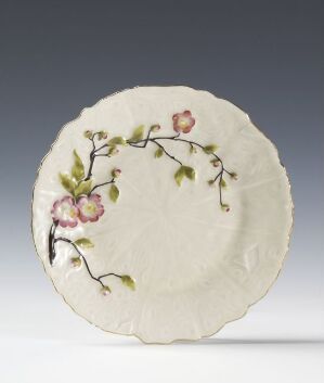  A hand-painted Feldspar porcelain plate with an organic edge by Porsgrunds Porselænsfabrik AS, decorated with a branch bearing leaves and blossoms in shades of green, pink, lavender, and yellow.