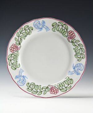  A round feldspar porcelain plate designed by Oluf Wold-Torne with a glossy finish featuring a hand-painted overglaze decoration of green leafy garlands, deep pink fruit or berry clusters, and delicate blue flowers around the rim, against a plain white center.