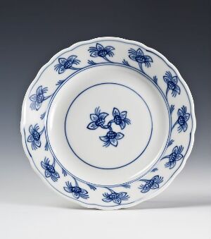  A white porcelain plate with a scalloped edge, featuring a cobalt blue floral pattern around the rim and a smaller, symmetrical flower cluster in the center.