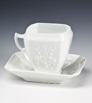  A white feldspar porcelain cup and saucer set with relief patterns, by Porsgrunds Porselænsfabrik AS, displayed against a grey gradient background.