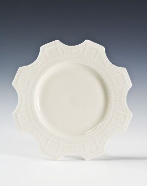  A decorative off-white plate with a starburst rim design on a gradient gray to white background.