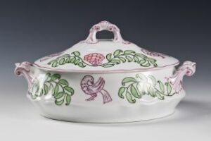  A white feldspar porcelain serving dish with hand-painted green, pink, and purple botanical motifs designed by Oluf Wold-Torne. The oval dish has an intricate lid with a pink knob and handles, reflecting a classic and ornate style.