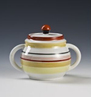  A feldspar porcelain sugar bowl by Porsgrunds Porselænsfabrik AS, featuring a white cylindrical body with horizontal stripes in yellow and brown, a round fitted lid with a red knob, and two side handles.