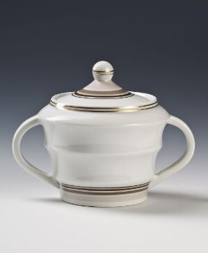  A white porcelain sugar bowl with golden and dark grey bands around the rim, designed by Porsgrunds Porselænsfabrik AS. It has a round body, two curved handles, and a removable lid with a round finial.