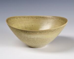  An earthy-toned ceramic bowl with a wide opening and shallow depth, featuring a glossy cream interior and a textured, speckled golden exterior that transitions to natural matte clay at the base.