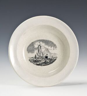  A creamy white ceramic plate with a glazed finish, featuring a central black-and-white illustration of a two-masted sailing ship on the sea, with a raised edge framing the maritime scene.