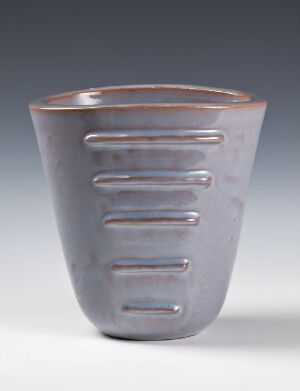  A ceramic vessel with a trapezoidal shape and flaring rim has a satin finish in shades of lavender and pale blue, featuring seven horizontal grooves around the body against a light gray background. The artist's name and title are unknown.