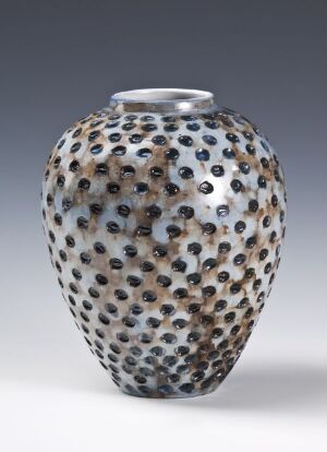  A decorative vase with a speckled pattern of earthy browns, beiges, greys, and occasional dark spots on a translucent white or light grey surface, featuring circular indentations, against a neutral background.