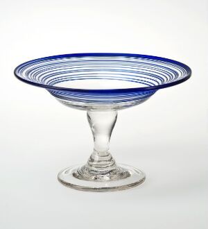  A shallow glass bowl with a stem foot, featuring concentric blue stripes around the rim, against a white background.