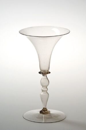  An elegant translucent glass goblet with a wide, flaring bowl and a stem featuring bulbous elements, against a soft white to light gray gradient background.