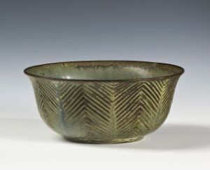  An ancient-looking olive green bowl with a pattern of engraved chevrons around the exterior, positioned against a light background.