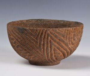  A small round brown textured bowl with geometric patterns etched onto the outer surface, set against a neutral gray background.