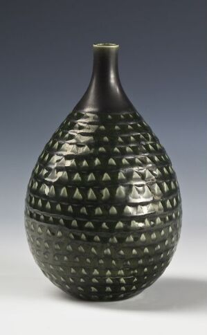  A pear-shaped, textured vase with a pattern of symmetrical indentations, displaying a lustrous deep green color against a plain gray background. Artist name and title are unknown.