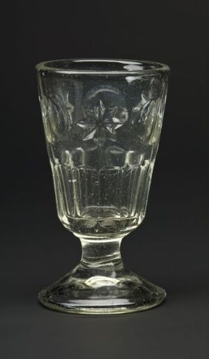  A transparent, etched glass goblet on a dark grey background, displaying intricate floral designs and reflecting subtle light.