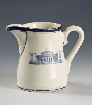  A cream-colored ceramic pitcher titled "Stortinget" by Egersunds Fayancefabrik, with a blue and golden trim around the rim and a blue transfer print of a building on the side.