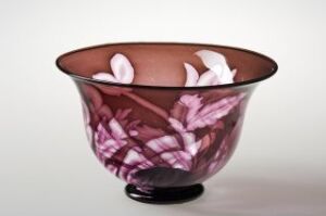  A handcrafted glass bowl on a neutral background, chocolate brown in color with a gradient towards transparency, featuring delicate white and purple floral motifs inside.