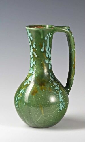  An antique green glass pitcher with a textured dot pattern, curvy handle, and a glossy finish, set against a neutral background.